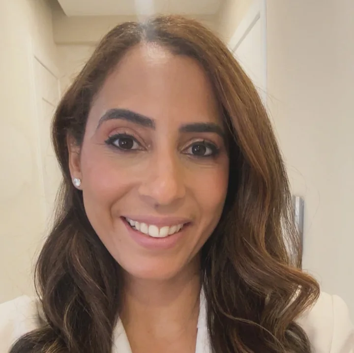 Erika Espinal sorrindo, usando um blazer branco